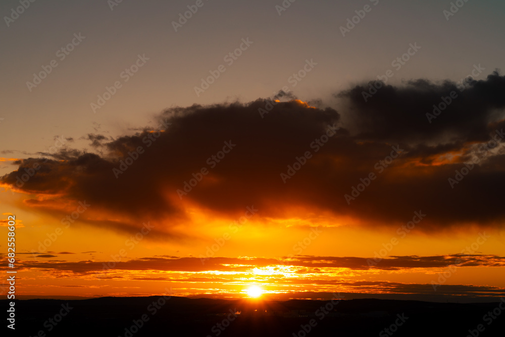 Marvellous sunrise in the sky in yellow, orange, red color palette with the dark giant cloud above the land. The view can be consider as sunset as well.