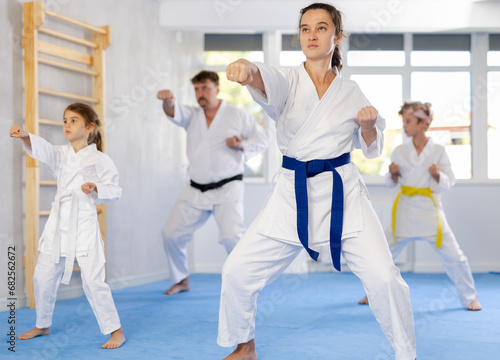 Experienced female karateka demonstrating kata sequence of movements to preteen daughter and son emphasizing hand striking techniques during family martial arts training ..