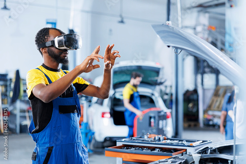 Expert in auto repair shop using virtual reality to visualize car ignition system in order to fix it. BIPOC experienced garage worker wearing futuristic vr headset while working on faulty vehicle