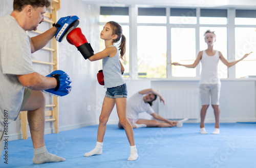 Father and girl engaged during training, boxing classes. Parent helps his daughter master basic wrestling skills. Parent coach in teaches child protection during wrestling and dueling, martial arts