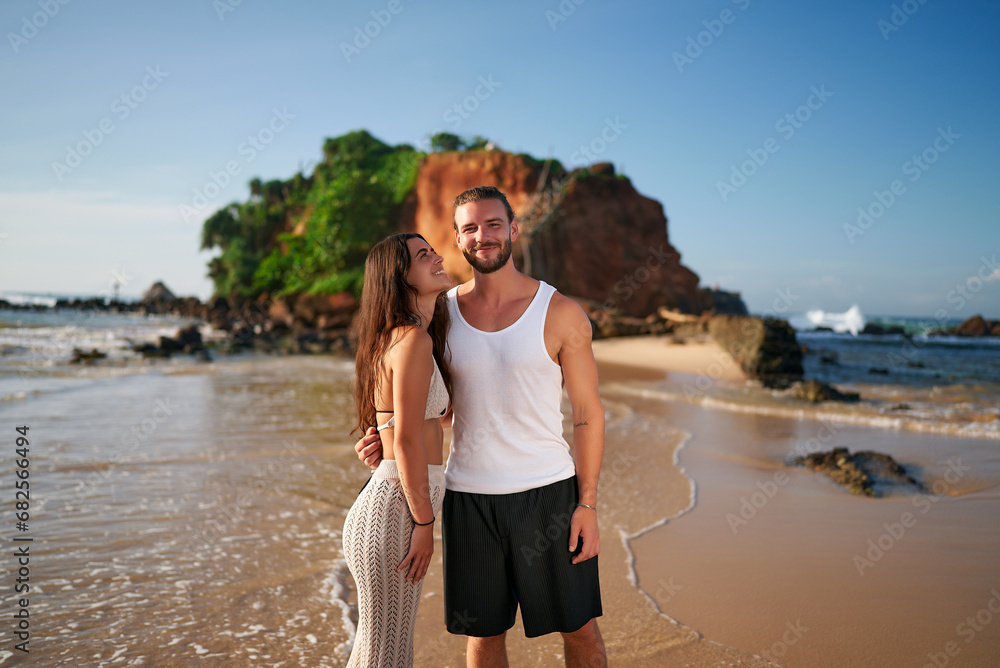 Happy couple embracing on sandy beach during sunset. Man and woman enjoy romantic tropical getaway. Vacation, love, travel, and leisure concept. Smiling tourists by the sea, summer holiday. Happy couple embracing on sandy beach during sunset. Man and woman enjoy romantic tropical getaway. Vacation, love, travel, and leisure concept. Smiling tourists by the sea, summer holiday.