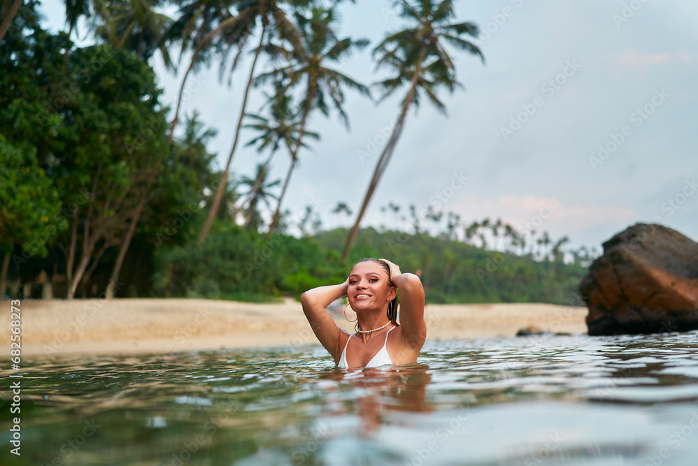 Fototapeta premium Woman enjoys serene swim in ocean at twilight, travel leisure concept. Female bather relishes peaceful sea dip, coastal sunset backdrop. Solo traveler experiences tranquil seawater, dusk ambiance.