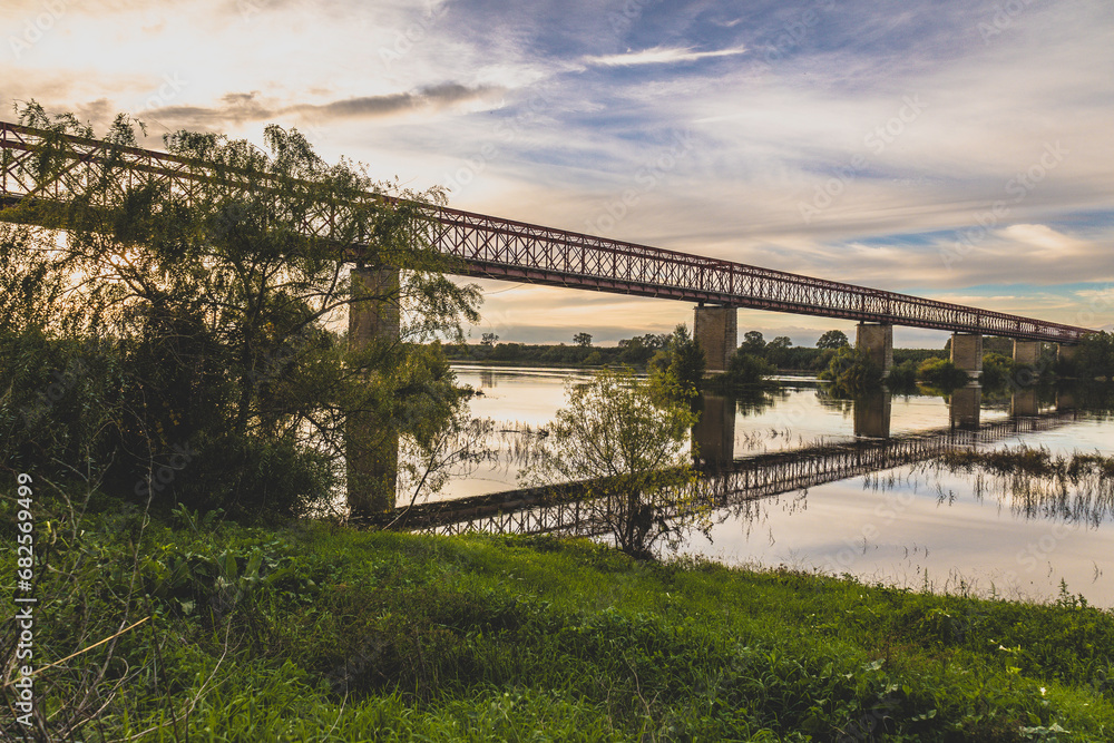 Fototapeta premium Old steel bridge at sunset. Bridge over the Tagus river, in the portuguese village of Chamusca - Ribatejo - Portugal. Bridge Isidro dos Reis - Chamusca