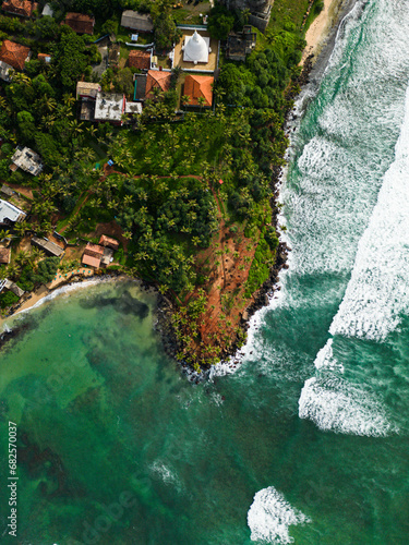 Aerial view from above of lush tropical coastal landscape and vibrant turquoise sea with white-capped waves. Tranquil bay, a traditional village temple, exotic travel destinations nature beauty. photo