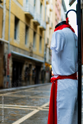 Empty street: mannequin dons San Fermin costume in red and white, cloudy day.