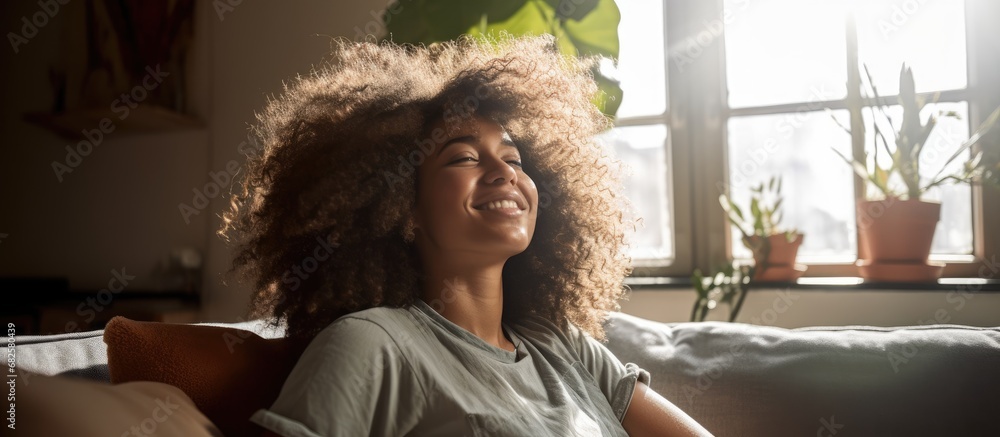 In her cozy African apartment, a young woman with a radiant smile enjoys a day of relaxation on her sofa, happy to be home, feeling the warm embrace of her hair against her face, embracing a fun and In her cozy African apartment, a young woman with a radiant smile enjoys a day of relaxation on her sofa, happy to be home, feeling the warm embrace of her hair against her face, embracing a fun and