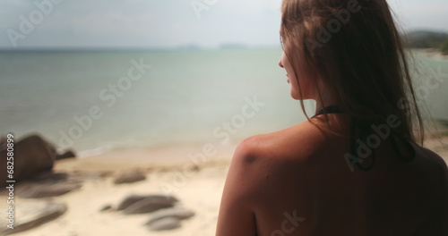 Woman relaxes on balcony on tropical island resort. Luxury spa apartment first line with beautiful seaside view. Back view long hair girl in bikini standing on terrace looking ocean waves. © Anastasia Pro