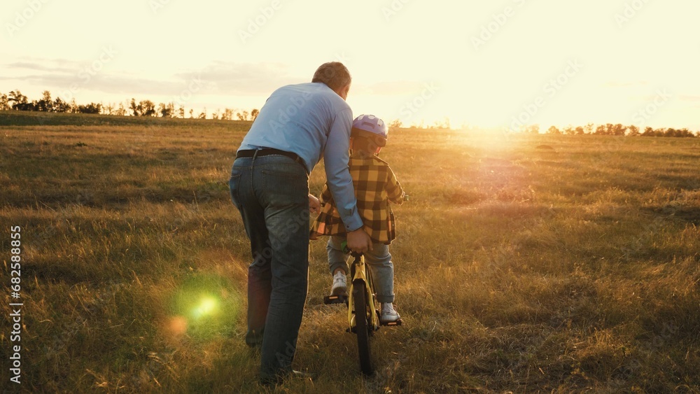 Supportive father gives gentle push to help persistent son steer bicycle - obrazy, fototapety, plakaty 