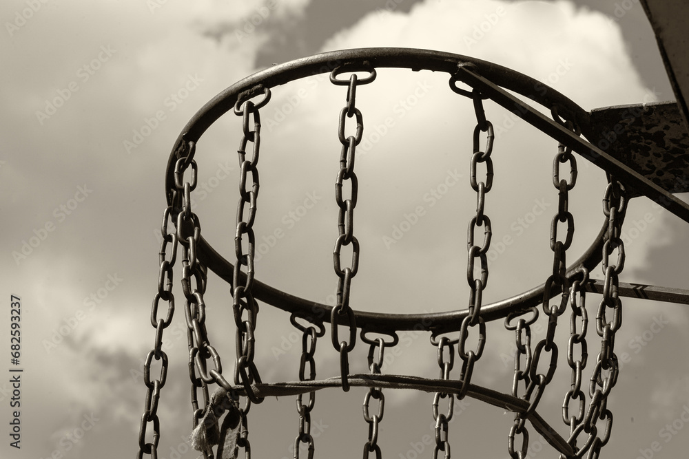 In a big city, between multi-story buildings, boys made a net for a basketball ring out of chain. In a big city, between multi-story buildings, boys made a net for a basketball ring out of chain.