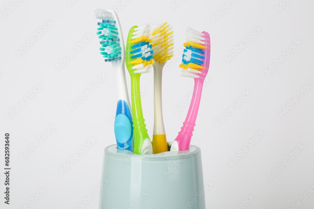 Different toothbrushes in holder on light grey background, closeup Different toothbrushes in holder on light grey background, closeup
