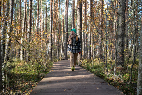 Woman tourist traveler walking on ecotrope in Scandinavian pine tree forest enjoying nature park. Relaxed middle aged female exploring woodland. Outdoor activity, tourism travel wanderlust concept.
