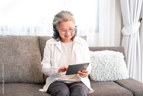 asian senior woman sitting on couch,relaxing in the living room,using internet online on tablet computer to communicate with her family,concept of elderly people modern life on technology