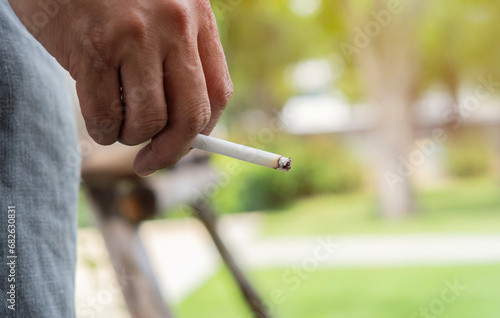 Image of cigarette in man hand with smoke while standing at outdoor.