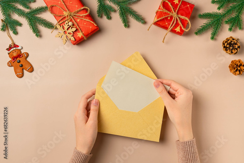 Envelop in woman's hands with blank of Christmas greeting card flat lay