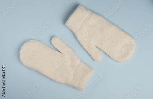 Warm white winter mittens on blue background. Top view, flat lay.