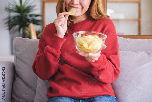 Closeup image of a young woman picking and eating potato chips at home