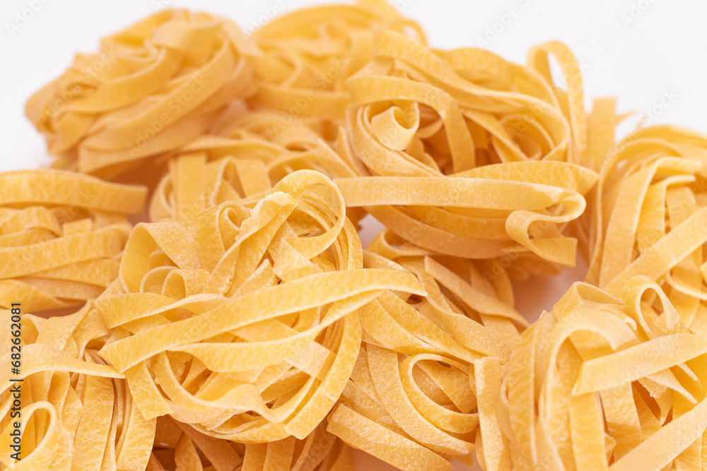 Scattered Classic Italian Raw Egg Fettuccine on White Table. Dry Twisted Uncooked Pasta. Italian Culture and Cuisine. Raw Golden Macaroni Pattern Scattered Classic Italian Raw Egg Fettuccine on White Table. Dry Twisted Uncooked Pasta. Italian Culture and Cuisine. Raw Golden Macaroni Pattern