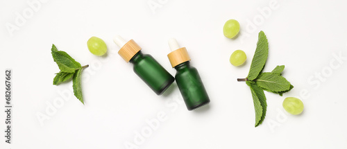 Bottles of essential oil, ripe grapes and mint leaves on white background