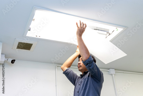Technician holding recessed mounted luminaire in ceiling house to repair or maintenance and fixing. Office building or house problem from electric light lamp for repairman change fluoresce light. photo