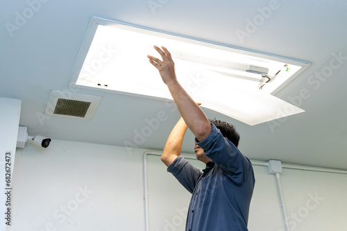 Technician holding recessed mounted luminaire in ceiling house to repair or maintenance and fixing. Office building or house problem from electric light lamp for repairman change fluoresce light. photo