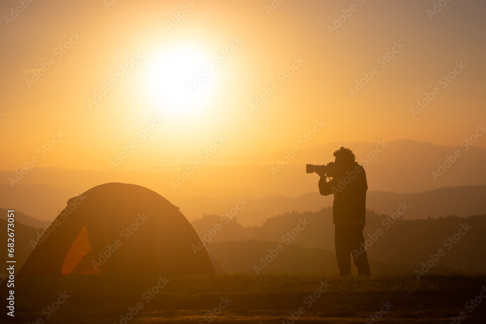 Photographer is taking landscape photo by the tent during overnight camping at the beautiful scenic sunrise over the mountain for outdoor adventure vacation travel