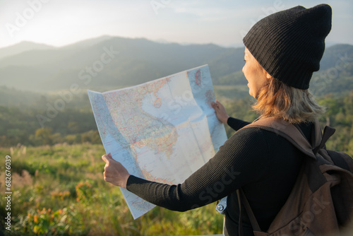 Adventurous girl navigating in with a topographic map in beautiful mountains of thailand. woman wearing hat stand alone and enjoying freedom and calm inspired travelling on background view mockup.