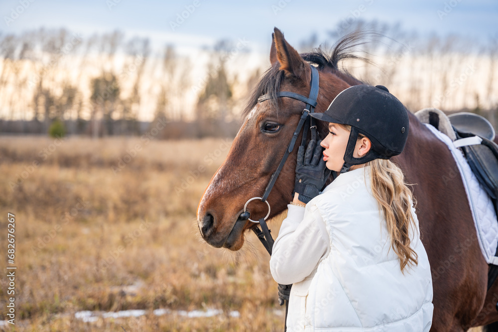 Obraz premium Beautiful blond professional female jockey standing near horse in field. Friendship with horse