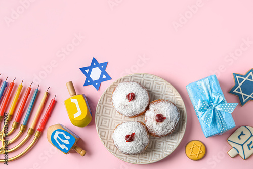 Menorah, dreidels, cookies, plate with donuts and gift box for Hanukkah celebration on pink background photo
