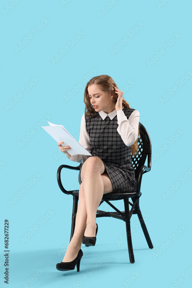 Beautiful actress with film script in chair on blue background Beautiful actress with film script in chair on blue background