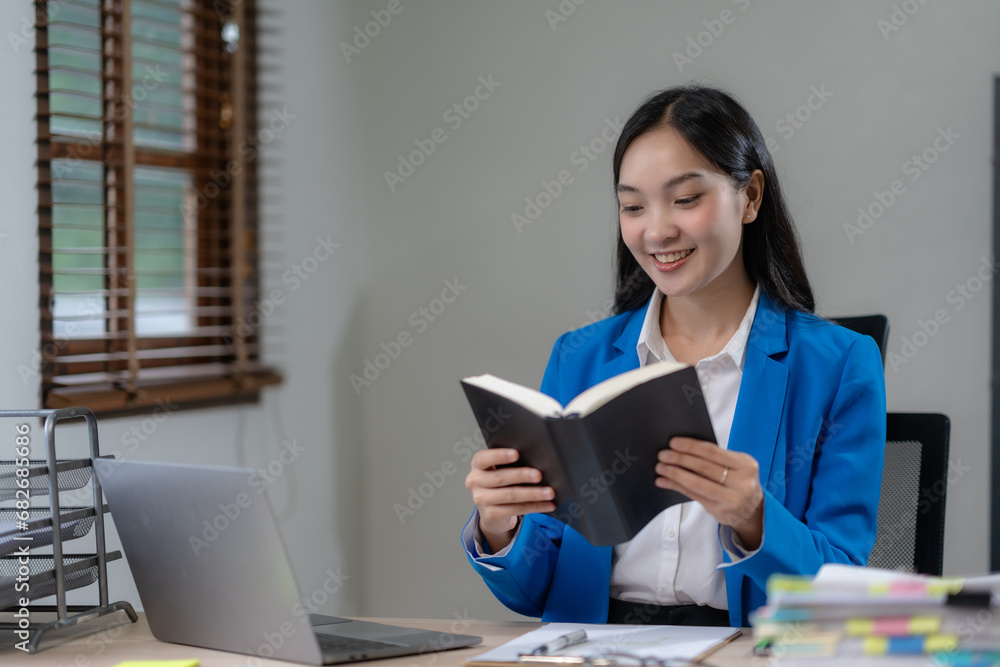 Financier working with documents at workplace. Young Asian business woman sitting working in modern office with documents and laptop computer. Financier working with documents at workplace. Young Asian business woman sitting working in modern office with documents and laptop computer.