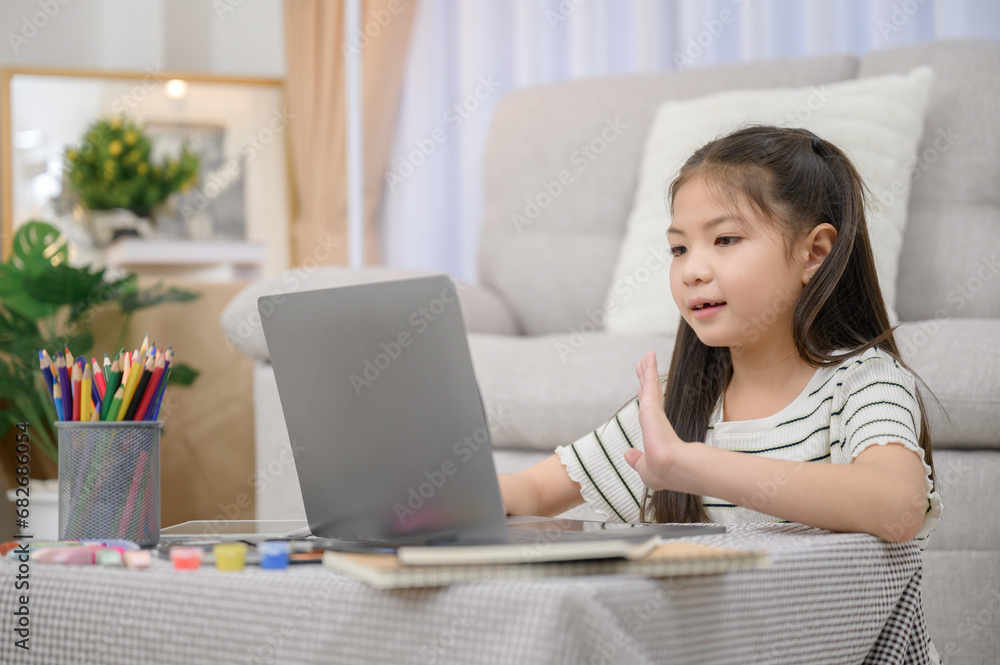A little Asian girl enjoying holiday activities. For education and learning that is fun and happy with using a laptop computer in the living room at home A little Asian girl enjoying holiday activities. For education and learning that is fun and happy with using a laptop computer in the living room at home