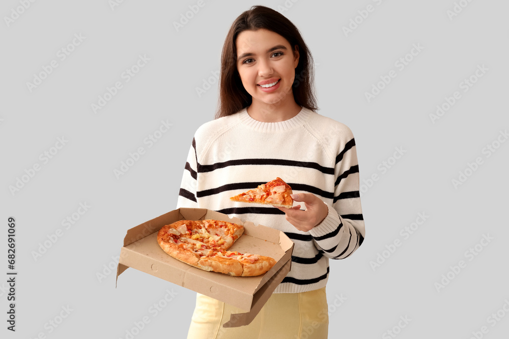 Young woman holding cardboard box with tasty pizza on grey background