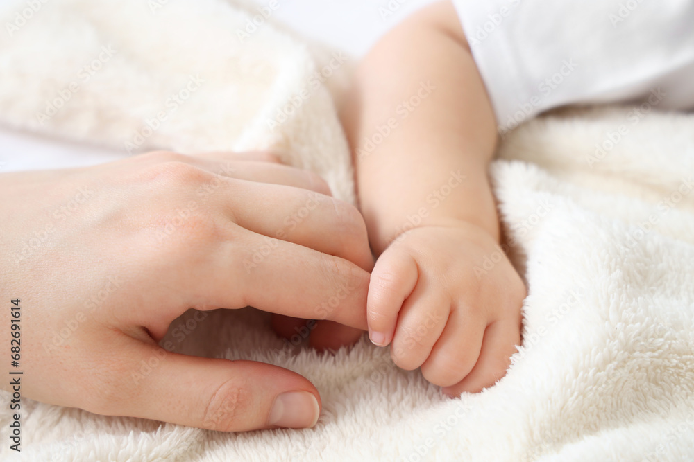 Mother holding her little baby's hand in bedroom, closeup Mother holding her little baby's hand in bedroom, closeup