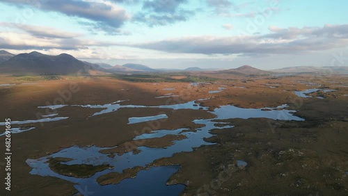 Wide drone shot of Connemara Lakes with calm lakes in the foreground and Beanna Beola mountain range in the distance, slowly panning aerial shot photo