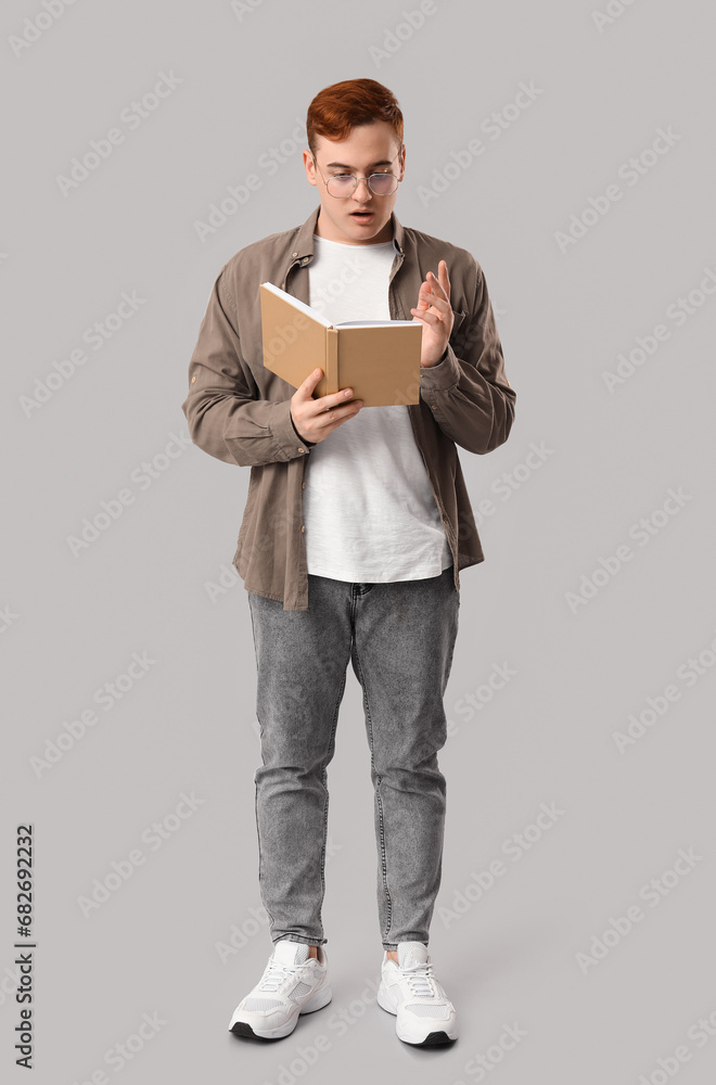 Emotional young man reading book on grey background Emotional young man reading book on grey background