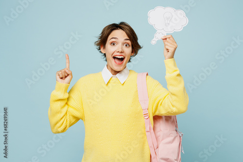 Young smart woman student wear casual clothes yellow sweater backpack bag hold say cloud with lightbulb point index finger up isolated on plain blue background. High school university college concept.
