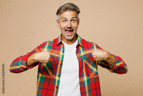 Adult surprised shocked fun man he wear red shirt white t-shirt casual clothes point index finger on himself isolated on plain pastel light beige color background studio portrait. Lifestyle concept.