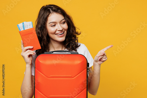 Traveler woman in casual clothes hold passport ticket bag point aside isolated on plain yellow orange background studio. Tourist travel abroad in free spare time rest getaway Air flight trip concept #682695206