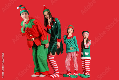 Happy family in elf's costumes showing silent gesture on red background