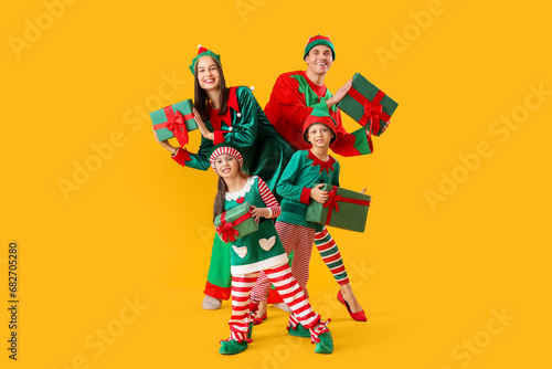 Happy family in elf's costumes with gift boxes on yellow background