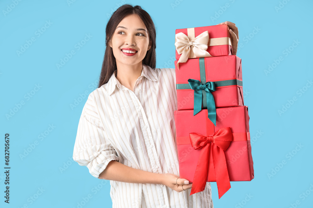 Beautiful young Asian woman with gift boxes on blue background Beautiful young Asian woman with gift boxes on blue background