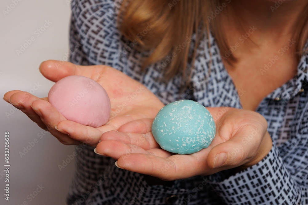 Japanese rice desert mochi closeup. Colouful mochi cakes in hands. Tasty fruit and chocolate mochi on grey background. Traditional cold ice asian candy. Japanese rice desert mochi closeup. Colouful mochi cakes in hands. Tasty fruit and chocolate mochi on grey background. Traditional cold ice asian candy.