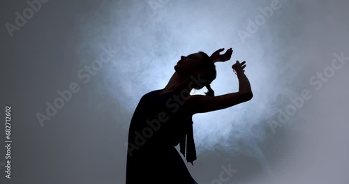 Graceful hard-working ballerina dancing in blue dress in studio in spotlight on black background. Diligent ballet dancer performing dancing elements of classical ballet, raising arms, bending back photo