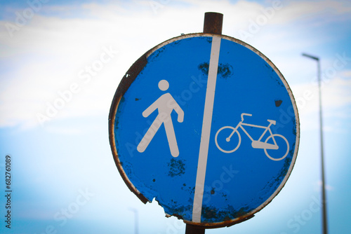 Cartello stradale rotondo blu, arrugginito, che indica una pista ciclabile divisa con i pedoni photo