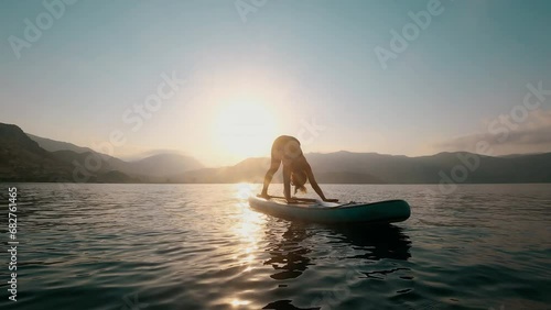 Young woman doing yoga on SUP board at sunset in slow motion photo