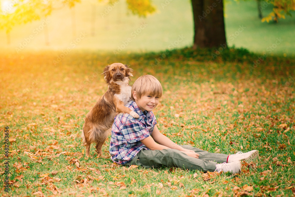 Fototapeta premium Boy hugging dog and plyaing with in the fall, city park
