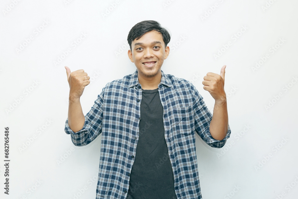 Portrait of young Asian Indonesian man smiling and showing two thumbs up as yes or successful gesture expression Portrait of young Asian Indonesian man smiling and showing two thumbs up as yes or successful gesture expression