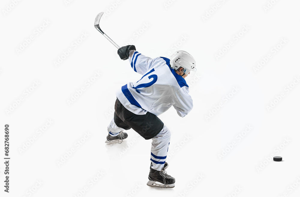 Young man, hockey player in motion during game, hitting puck with stick against white studio background. Scoring goal