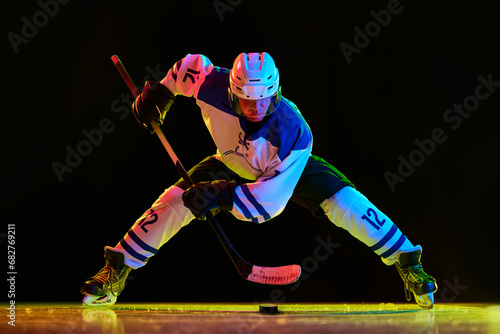 Canvas Print Young man, hockey player in uniform during game on rink, standing with stick and