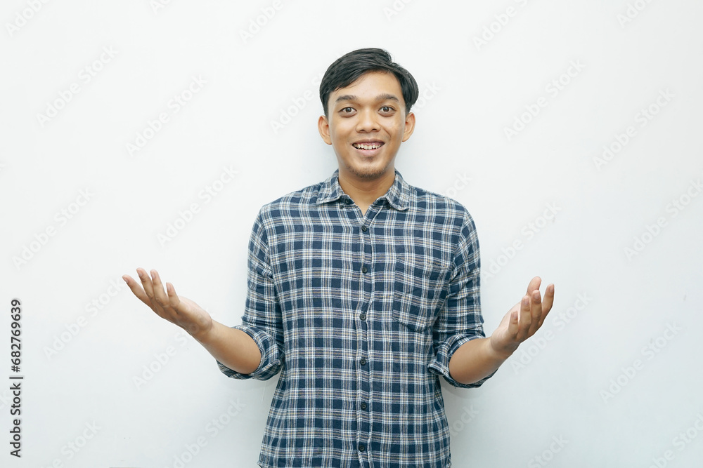 Portrait of young Indonesian Asian man smiling while put hand palms in front of his body for presenting something gesturing Portrait of young Indonesian Asian man smiling while put hand palms in front of his body for presenting something gesturing